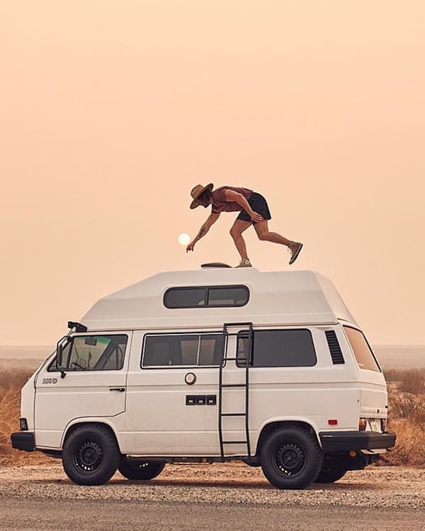 Life in the Slow Lane - @christiandelatorre_ 09/2022 Christian de la Torre (@christiandelatorre_) balancing on the roof of his iconic white 1984 VW Westfalia camper van, set against a serene desert sunset. The van, equipped with a high-top roof and side ladder, embodies the adventurous spirit of the van life lifestyle. Christian is seen playfully reaching toward the setting sun, capturing the essence of exploration and freedom central to his van life journey.