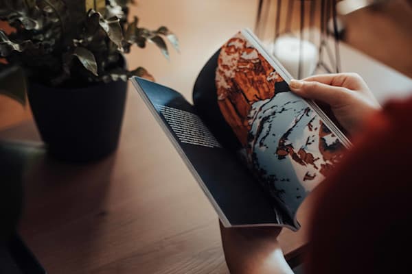 The roadoffice magazine - @hypespeed 09/2022 @hypespeed’s hands hold an open copy of Roadoffice Magazine, flipping through a page featuring a breathtaking photograph of a snow-covered mountain landscape. The magazine’s high-quality print showcases detailed imagery and engaging text, embodying themes of travel, adventure, and remote work. The scene is set in a cozy indoor space with a wooden table, a potted plant, and soft ambient lighting, creating a relaxed and inspirational atmosphere. This moment captures the tactile experience of reading Roadoffice Magazine, reinforcing its focus on van life, overlanding, and the freedom of working from anywhere.