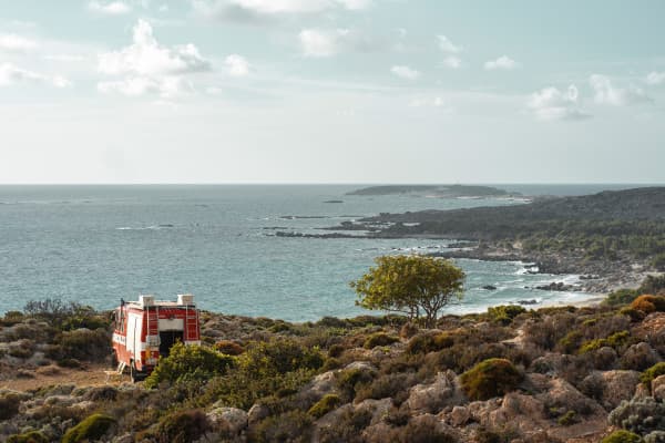 Beautiful and diverse, but also very exhausting - @hummel_die_feuerwehr 06/2022 A red firetruck, @hummel_die_feuerwehr, converted into a camper, parked on a rocky coastline overlooking the sea, highlighting the vanlife experience in a remote coastal location on Crete’s south coast.