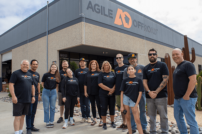 The Agile Offroad team in front of their headquarters - @deafroamer 06/2025 Gregg Pappas, also known as @deafroamer on Instagram, stands with the Agile Offroad team in front of their headquarters, celebrating his role as a brand ambassador and advocate for accessible vanlife. Wearing matching Agile Offroad shirts, the diverse group of men and women pose together outside the industrial-style building with the company’s bold orange and gray logo above the entrance. This image captures the spirit of collaboration and inclusivity between a deaf vanlifer and a leading off-road vehicle outfitter, emphasizing shared values of community, innovation, and support for the deaf and hard of hearing in the vanlife and overland travel space.