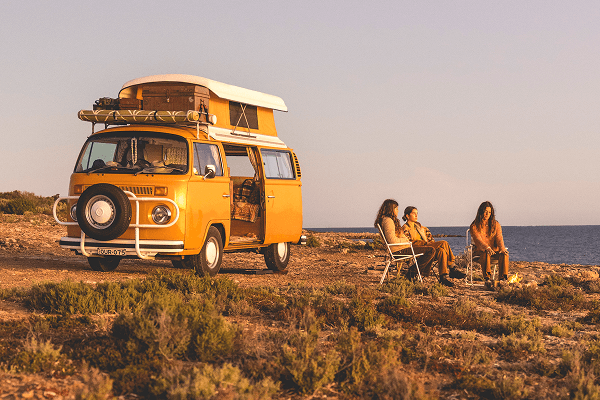 The perfect shade of mellow yellow - @summerofseventyfive 12/2022 The summerofseventyfive family relaxes beside their bright yellow 1975 Volkswagen Kombi camper van with a pop-top roof, parked on a rugged coastal bluff in Australia during golden hour. The van is loaded with camping gear on the roof rack, and the side door is open. The family sits in folding chairs around a small campfire, enjoying the warm light of sunset with the ocean stretching out behind them, capturing the spirit of vanlife, family adventure, and off-grid coastal travel.