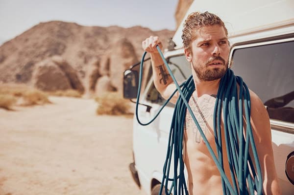 Life Rips - @christiandelatorre_ 09/2022 Christian de la Torre (@christiandelatorre_) stands shirtless next to his 1984 VW Westfalia camper van, holding a coiled climbing rope over his shoulder in the rugged desert landscape of Joshua Tree, California. The sunlit scene highlights his adventurous spirit and connection to outdoor exploration, a central theme in his van life lifestyle. With rocky formations in the background, this image encapsulates the freedom and resilience described in his article about living on the road and embracing the unexpected.