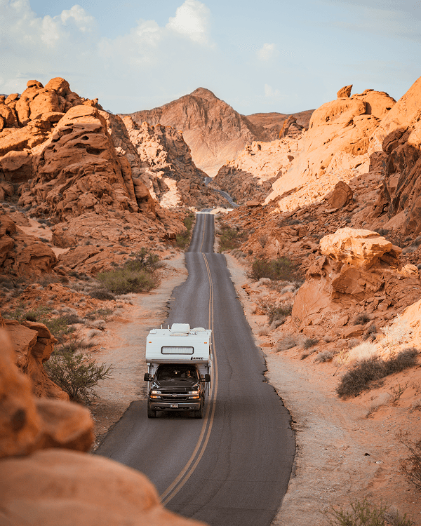 Exploring the Valley of Fire State Park, Nevada - @on.vagabonde 03/2023 A Chevrolet truck camper with a Lance camper shell named Jeff drives along a winding desert road through dramatic red rock formations in Valley of Fire State Park, Nevada, captured by on.vagabonde during their Pan American Highway vanlife journey.