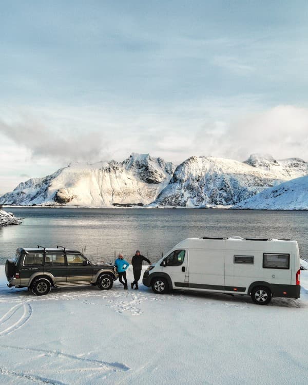The beauty of the Arctic - @travelvan 08/2021 Winter adventure in Northern Norway with a campervan and SUV parked by a serene snowy lake surrounded by stunning snow-capped mountains. Capturing the essence of travel and exploration in the Arctic by @travelvan.