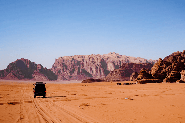 A glimpse of all the beautiful experiences - @countless_roads 03/2023 The Mitsubishi L300 4x4 of @countless_roads driven by Amy and Jeroen crosses the red sand desert of Wadi Rum in Jordan, leaving fresh tire tracks toward towering sandstone mountains under a clear blue sky. The image reflects the essence of vanlife, overlanding freedom, and adventure travel across the Arabian landscapes.