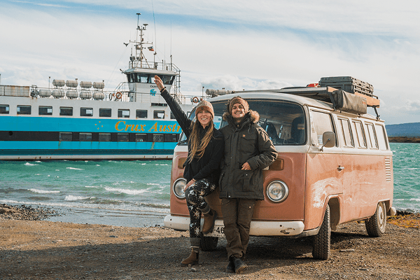 We made it to Puerto Natales, in the Magallanes region - @octaviaviajando 09/2022 Victoria from Chile, known as @octaviaviajando, stands with her partner next to their pink and white 1985 Volkswagen Kombi on the windy shores of southern Chile. The couple smiles in warm jackets, with a large blue and white ferry named Crux Australis docked behind them on turquoise waters. Captured during their vanlife journey through Patagonia, this image reflects their adventurous spirit, nomadic lifestyle, and love for nature and slow travel across remote regions of the country.
