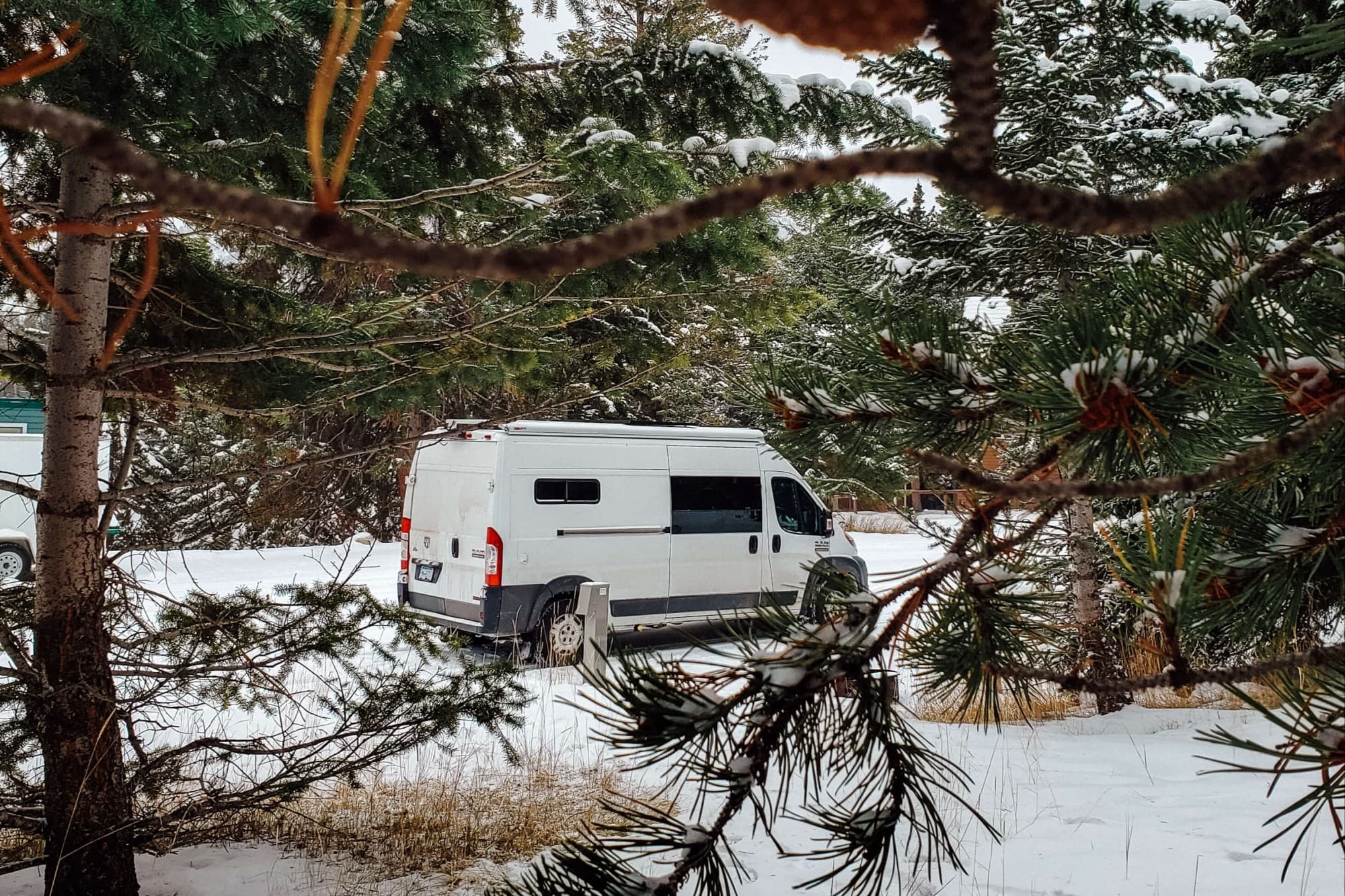Emily's Ram Promaster in the Canadian Winter - @emsvanlife 08/2021 White RAM van parked in a snowy forest setting in Canada, surrounded by pine trees. The image captures the essence of vanlife during winter, highlighting the challenges and beauty of living in a van amidst nature.
