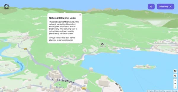 3D view near lake Bled in Slovenia with a "Natura 2000" pop-up - vanlifezone.com/map 3D interactive map view from Vanlifezone near Lake Bled in Slovenia, highlighting a Natura 2000 Zone in Julijci. The map shows rolling green hills and a large blue body of water with a pop-up information box describing the area's environmental significance and camping regulations. It includes the names of local rivers like Sava Dolinka, roads, and landmarks. A 'Camp Site' icon indicates a nearby camping area. The map features user interface elements like a 'Close map' button, and zoom controls, with Mapbox and OpenStreetMap credits in the corner.