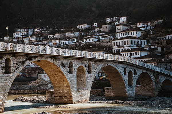 Historic Stone Bridge in Berat, Albania - @edelweiss.on.the.road 06/2022 This image captures the historic stone bridge in Berat, Albania, with the town’s iconic white Ottoman-era houses climbing the hillside in the background. It highlights Thomas & Regina’s exploration of Albania’s rich cultural heritage during their vanlife journey with @edelweiss.on.the.road.